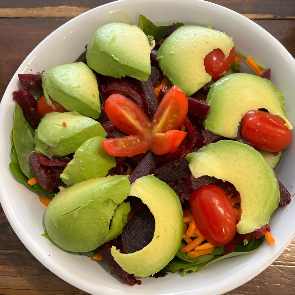 A vibrant salad with sliced avocado, cherry tomatoes, and shredded beets in a white bowl.