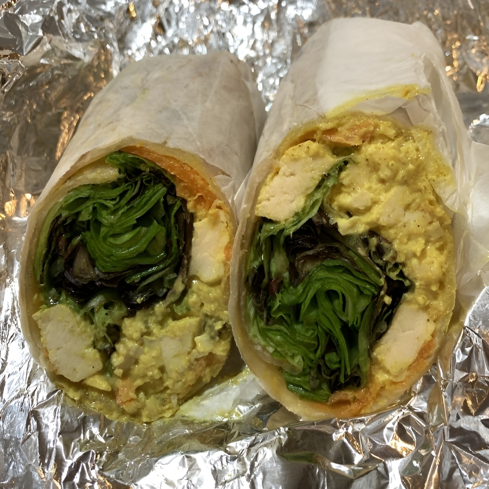 Two halves of a chicken salad wrap with lettuce and carrots, wrapped in paper and foil.