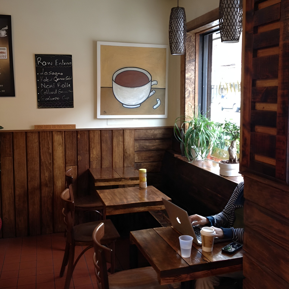 A person works on a laptop at a wooden table in a cozy cafe with a chalkboard menu.