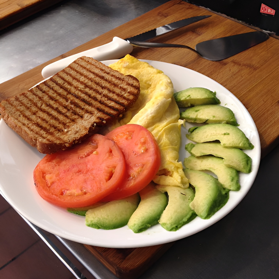 A healthy breakfast plate with grilled toast, scrambled eggs, sliced tomatoes, and avocado on a white plate.